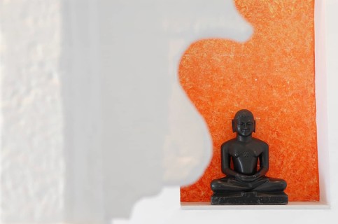 Statue of a black Buddha sitting meditating against an orange background, Devigarh Palace Hotel,