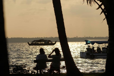 A couple sitting on a lakeside bench at sunset, boats gliding in the water, romantic atmosphere,