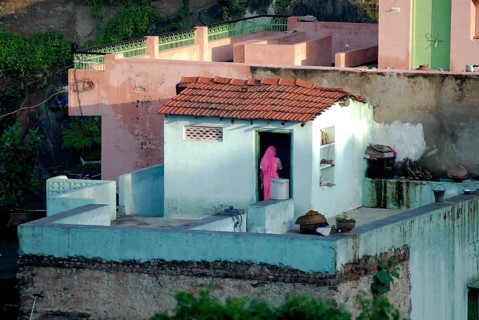 A woman wearing pink sari stands on the roof of a turquoise house, PDorf Delwara near Udaipur,
