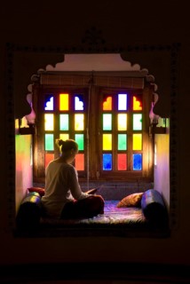 Woman sitting cross-legged reading in a room with colorful windows, calm and contemplative