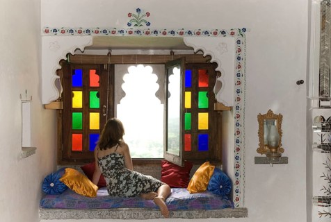 Woman wearing a dress in a cozy sitting area with pillows in front of colorful window, Palasthotel