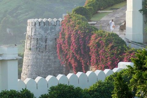 Hotel worker next to bougainvillea covered defensive defence tower in morning light, Devigarh