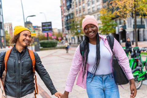Young multiracial couple smiling and holding hands while strolling down a city street lined with
