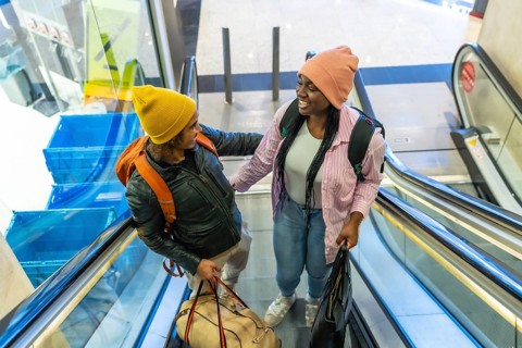 Diverse friends traveling together, smiling and feeling happy while riding escalator in airport or