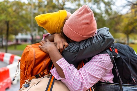 Two young adults are sharing a close, emotional embrace outdoors, holding onto each other with