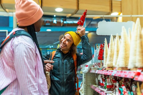 Diverse young couple laughing and shopping for festive holiday decorations in a bright store,