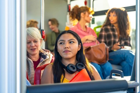 Young woman looking away while commuting on a bus with a diverse group of passengers, representing