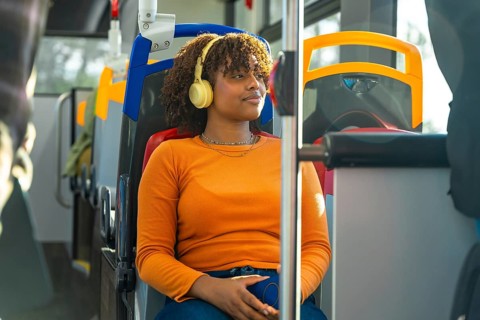 Young black woman with afro headphones relaxes and listens to music on a city bus during her