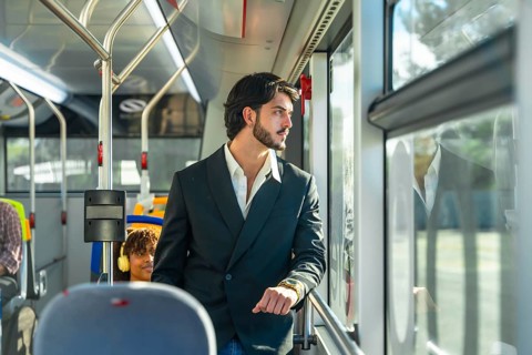 Young businessman in a suit jacket stands by a transit window, looking out pensively as the city
