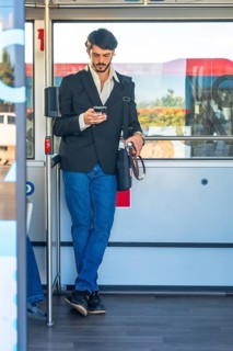 Young man standing on a crowded bus, absorbed in his smartphone as he scrolls and messages during a