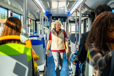Senior woman smiling and walking along the aisle of a public bus, passengers traveling and sitting