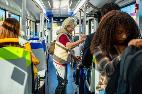 Senior woman standing inside a crowded city bus, holding a handrail among diverse commuters during