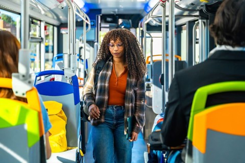 Young woman passenger with long curly hair and glasses walking along the aisle of a public bus,