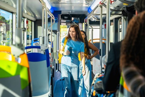 Young woman passenger holding a reusable coffee cup and backpack, walking through the aisle of a