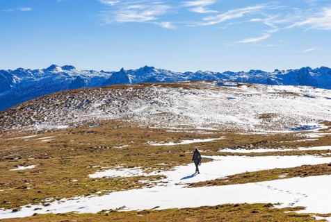 Female hiker walks across a snowfield on the Trattberg Alm with a view of the Tennengebirge,