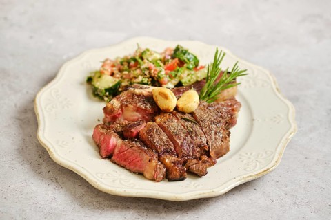 Juicy grilled steak on a vintage plate. Next to it, a vibrant tabbouleh salad features chopped