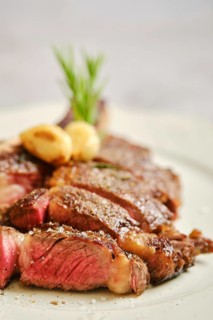Close-up view of cowboy steak slices on a white plate. The meat is seared to perfection, showcasing