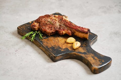 A juicy grilled cowboy steak on a rustic wooden cutting board. Garnished with fresh rosemary and