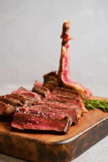 Thick slices of perfectly cooked t-bone steak medium rare on a wooden cutting board. Fresh herbs