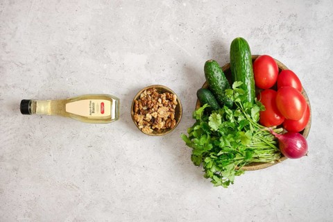A colorful arrangement of fresh tomatoes, cucumbers, and herbs on a light gray surface. A bowl of