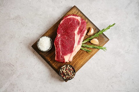 Raw ribeye roll steak rests on a wooden cutting board alongside garlic cloves and fresh rosemary.