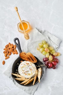 A cheese platter on a light background, showcasing a brie cheese wheel drizzled with honey.