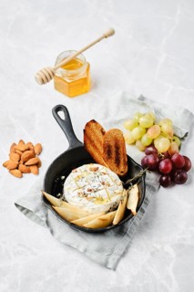 Soft brie cheese dish is baked in a small skillet, served with crispy bread, fresh pears, and