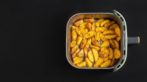 Top view of golden brown potato wedges in an air fryer basket against a dark background. These