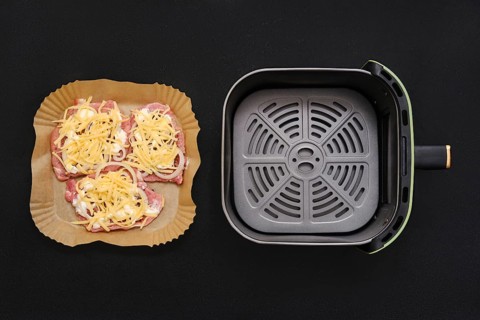 Three seasoned pork chops arranged on a parchment-lined tray, garnished with shredded cheese. Next