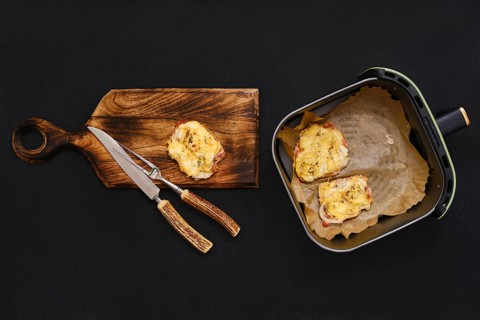 Golden-brown pork chops are placed on a wooden cutting board next to an air fryer