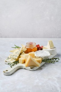 Fine selection of cheeses, honey, and herbs arranged artfully on a platter. Cubes of aged cheese,