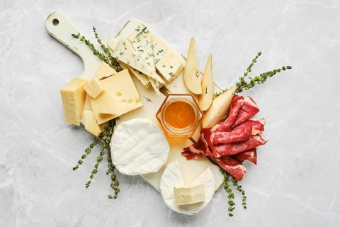 A beautifully arranged serving board features a variety of cheeses, cured meats, and fresh fruits.