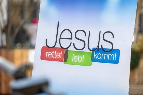 Sign with the inscription JESUS RETTET LEBT KOMMT at the information stand of a free church in