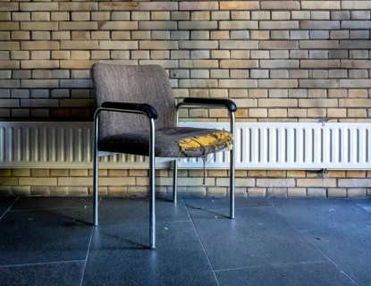 Retired and broken old office chair stands in front of a small radiator in an office building,