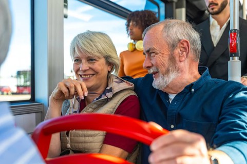 Senior husband and wife smiling and chatting on a daytime city bus, enjoying public transport
