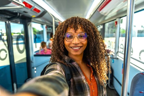 Young woman with curly hair and glasses smiling at camera while taking a happy selfie on a city