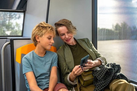 Mother and son sharing a smile as they browse a smartphone together on a city bus, enjoying a