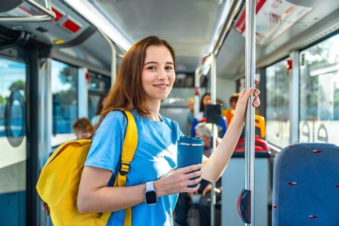 Young woman smiling on a city bus, standing and holding a pole with a yellow backpack and reusable