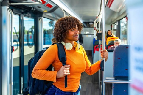 Young black woman with headphones and backpack standing in a public transport bus, holding a