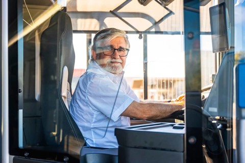 Senior man with a white beard and glasses wearing a shirt, sitting at the driver's seat of a modern