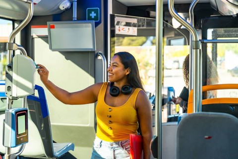 Young smiling woman using a payment validator for her ticket or travel card when boarding a city