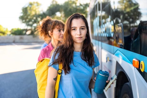 Young female commuters are standing in line, holding a reusable cup and a wallet, waiting to board