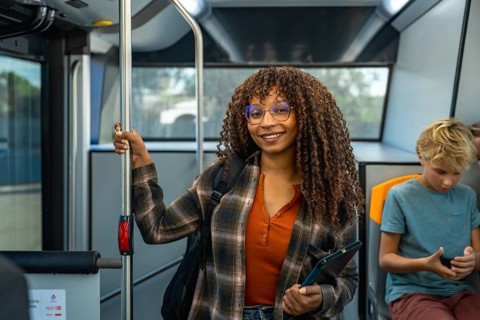 Young black woman with curly hair wearing glasses and a plaid shirt, smiling at camera, holding