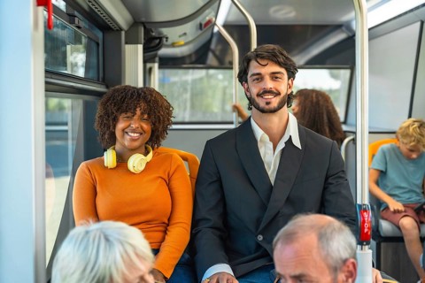 Diverse young couple smiling at camera while seated on a city bus, enjoying their commute and eco