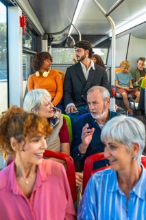 Multiethnic, multi generational passengers seated inside a city bus, chatting and commuting