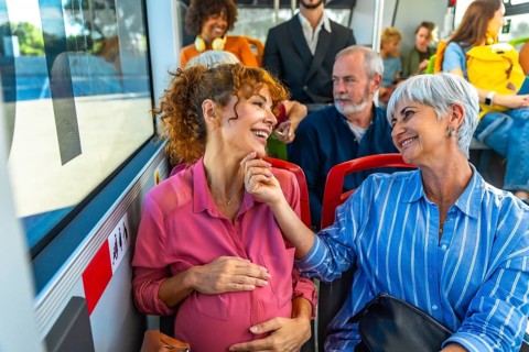 Pregnant woman and senior woman are smiling and talking while traveling on a public bus, sharing a
