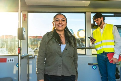 Smiling young woman standing inside a city bus during her daily commute, enjoying the ride while a