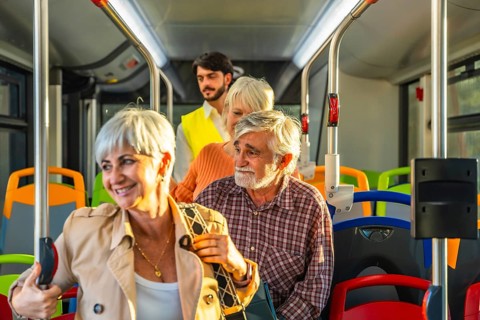 Seniors with gray hair and a younger man riding a modern public bus, holding onto vertical poles