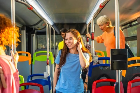 Diverse commuters stand and ride a bright city bus, holding handrails and chatting as they travel