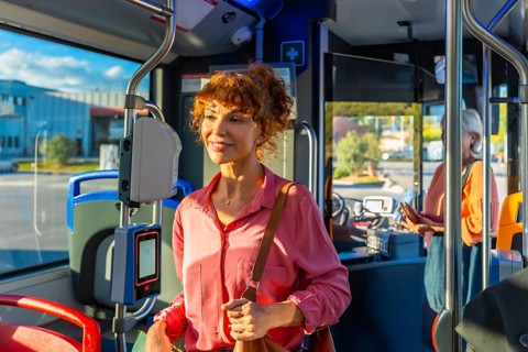 Smiling redhead woman validating a smart ticket on a modern city bus, preparing for her daily